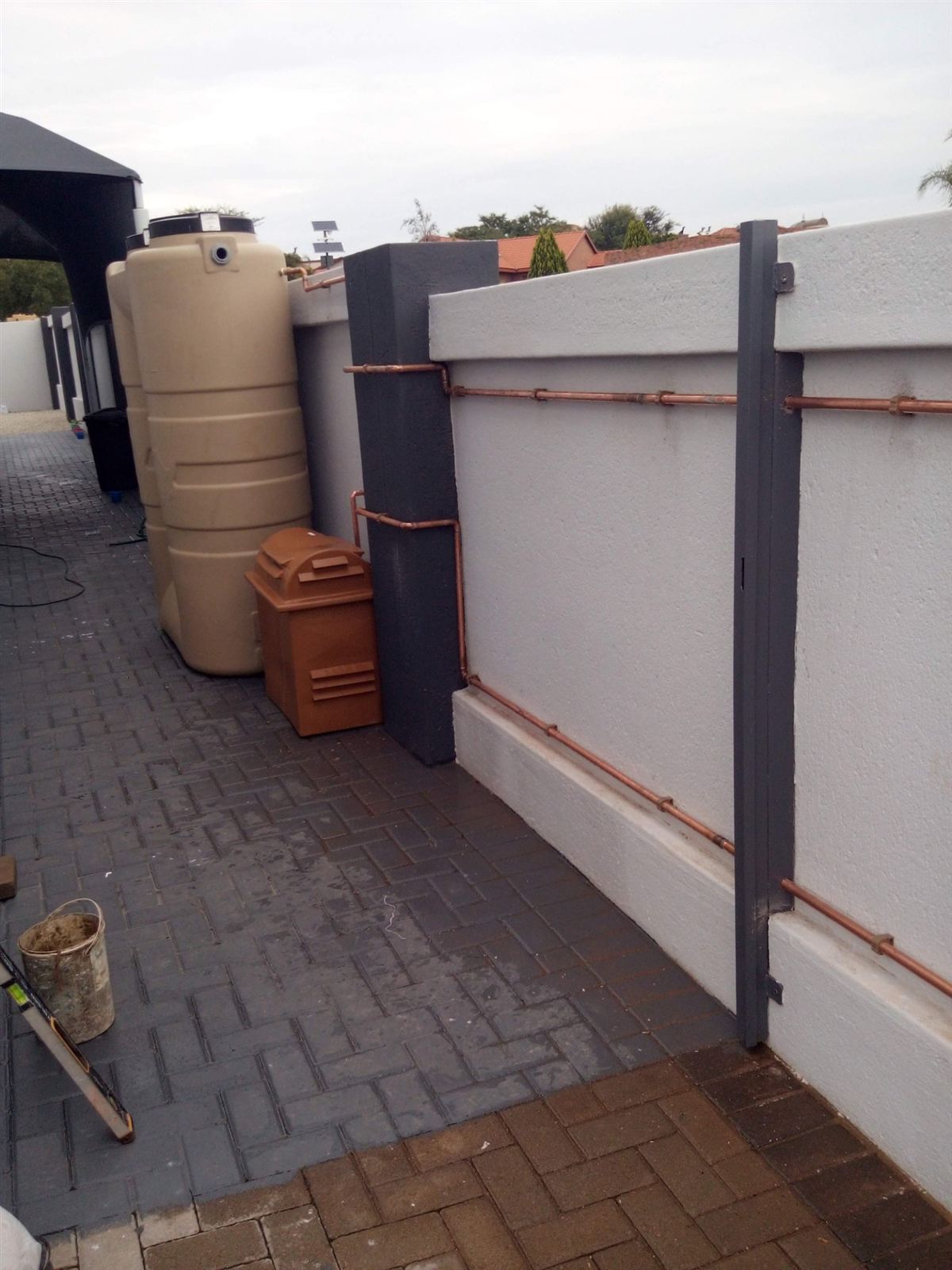 Two slim water tanks and a pump cover beside a boundary wall